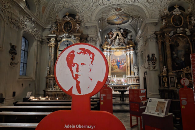 Porträt einer Frau auf roter Figur, im Hintergrund Kirchenraum