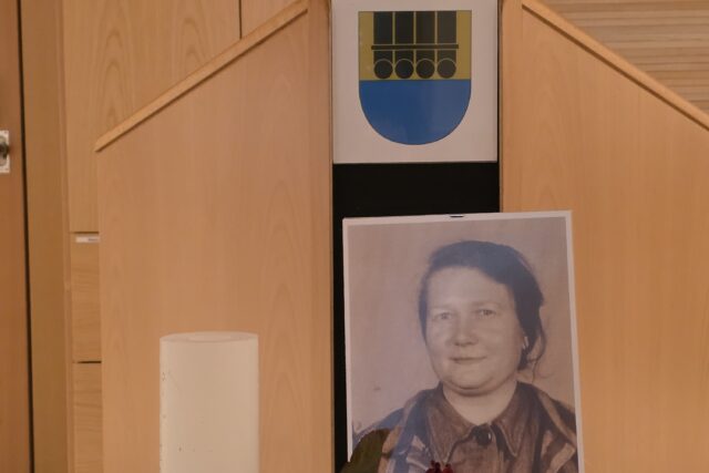 SW-Porträt einer Frau, daneben Kerze, Stacheldraht und Rose, darüber das Gemeindewappen von Mötz