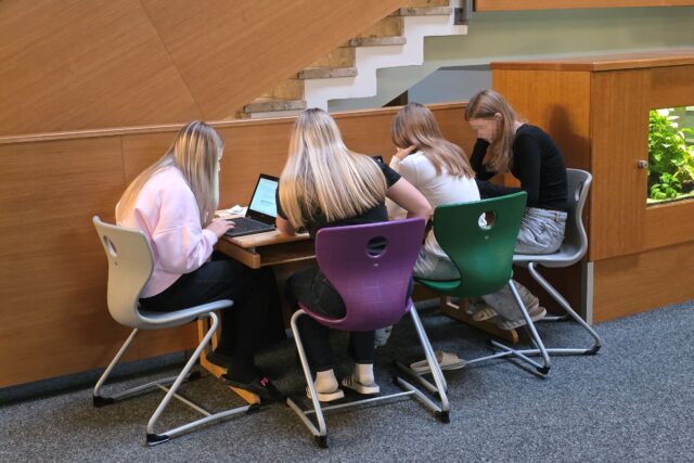 Schülerinnen an einem Tisch beim Recherchieren und Schreiben.